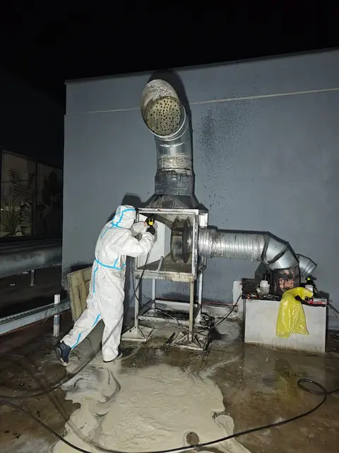 Tehnician în combinezon de protecție degresează noaptea carcasa ventilatorului de exhaustare pe acoperiș