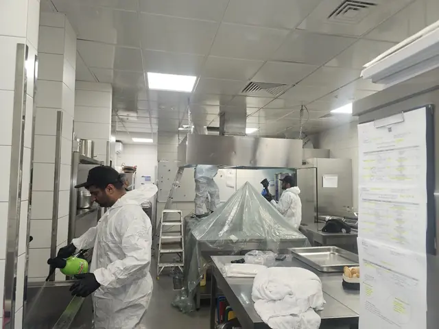 Echipă în combinezoane de protecție degresând o hotă centrală, cu utilajele de dedesubt acoperite cu folie