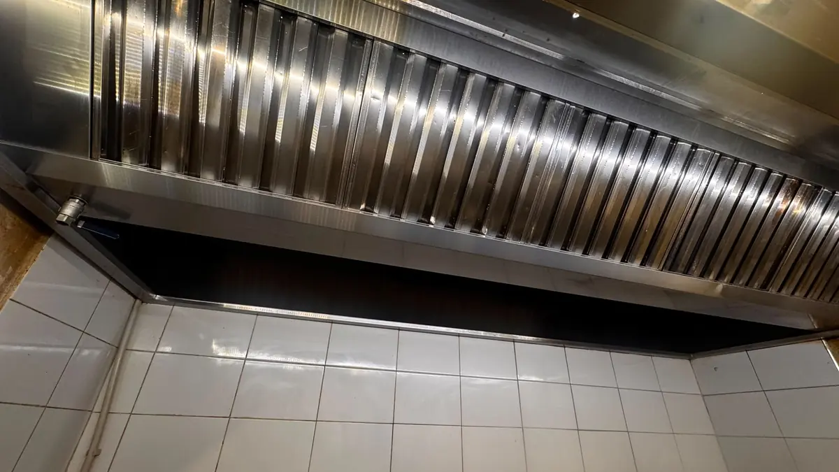 Filtre labirint din inox curate, montate pe toată lungimea unei hote profesionale, deasupra unui perete cu faianță albă
