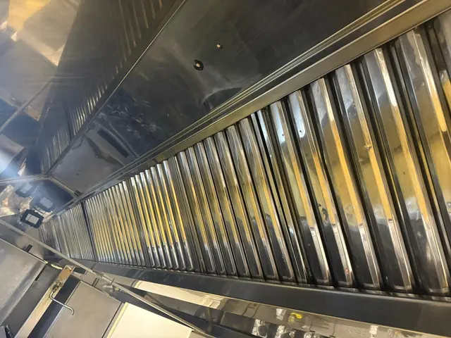 Rând lung de filtre labirint din inox strălucitoare, curățate, montate în hota unei bucătării profesionale