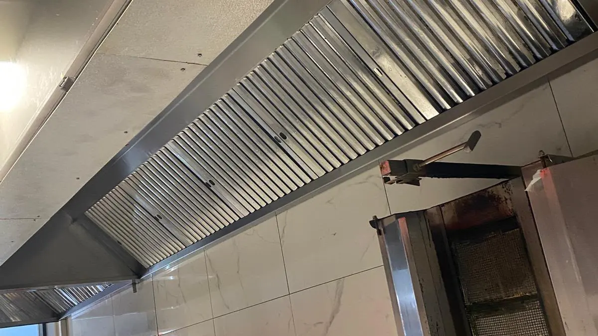Hotă profesională din inox cu filtre labirint curate, montată deasupra grătarului vertical într-un fast-food