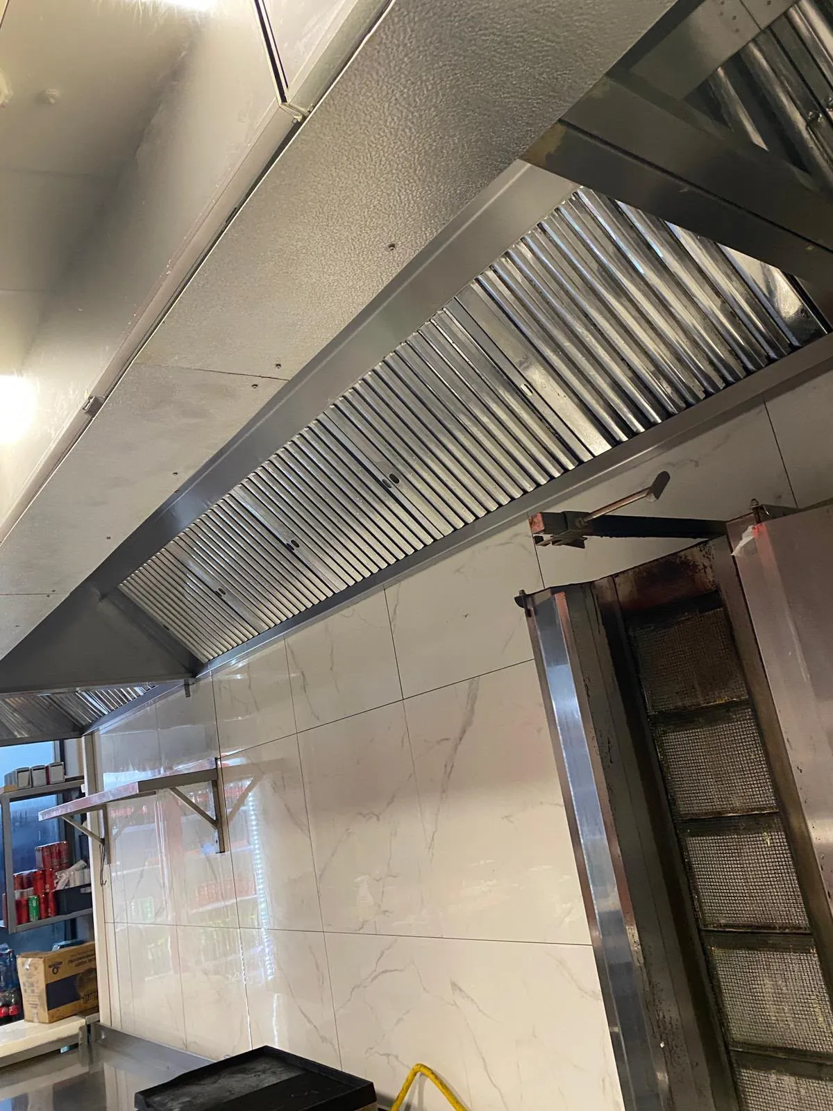 Hotă profesională din inox cu filtre labirint curate, deasupra grătarului vertical dintr-un fast-food