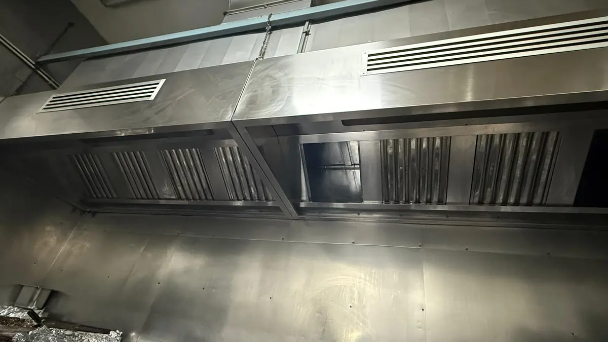 Hotă lungă din inox cu filtre labirint și grile de aer, curată după degresare, deasupra liniei de gătit