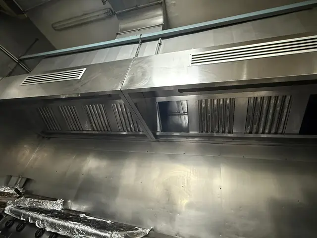 Hotă lungă din inox cu filtre labirint și grile de aer, curată după degresare, deasupra liniei de gătit