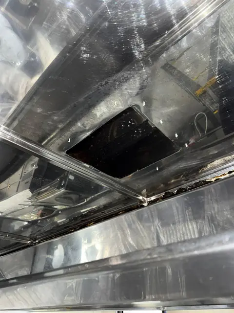 Plafonul hotei din inox văzut de jos, cu gura de evacuare dreptunghiulară și depuneri de grăsime în jgheab