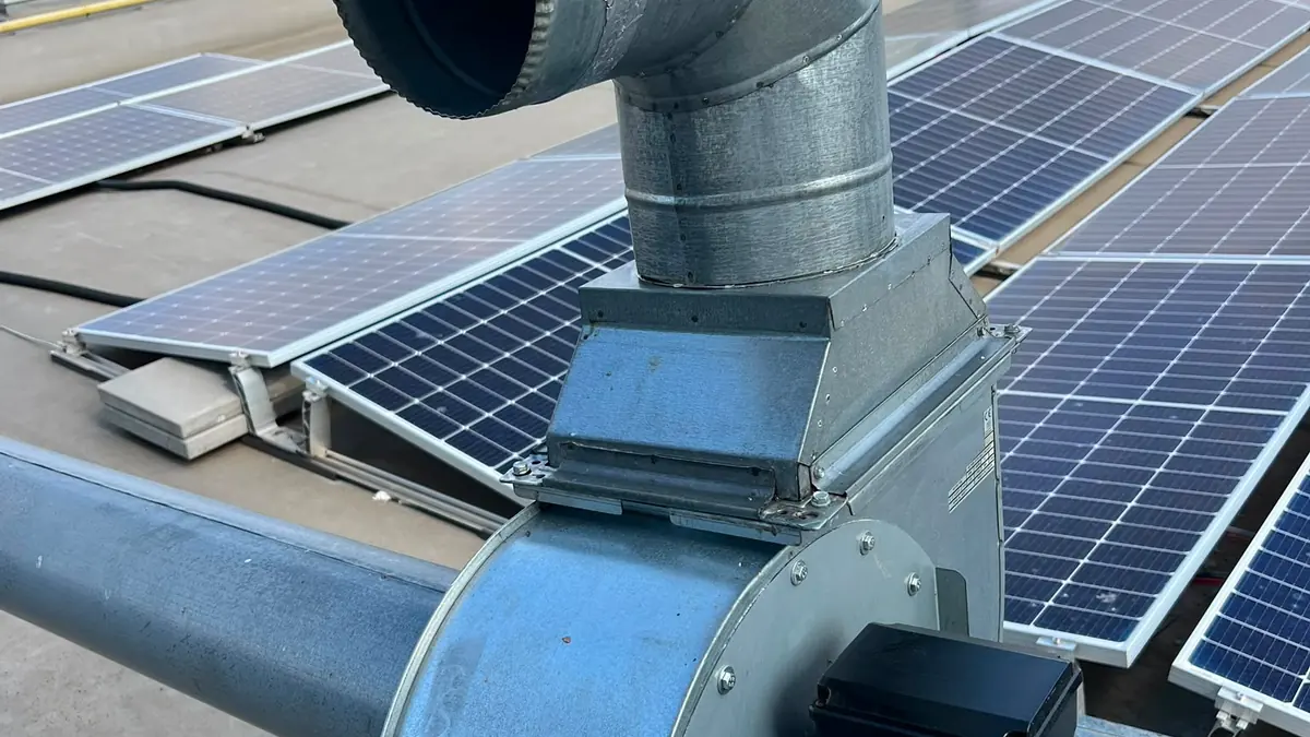 Ventilator centrifugal de exhaustare cu motor electric și cot de evacuare, montat pe acoperiș între panouri solare