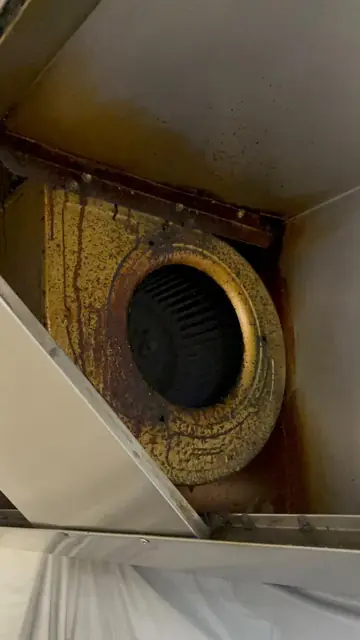 Ventilator centrifugal montat în interiorul hotei, cu carcasa acoperită de grăsime îngălbenită și scurgeri