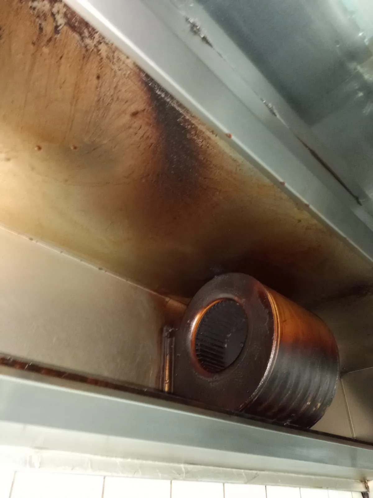 Ventilator centrifugal montat în plenul hotei, cu carcasa și pereții acoperiți de grăsime maronie, înainte de curățare